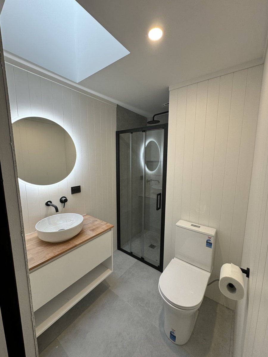 Bathroom with backlit round mirror, timber vanity and skylight