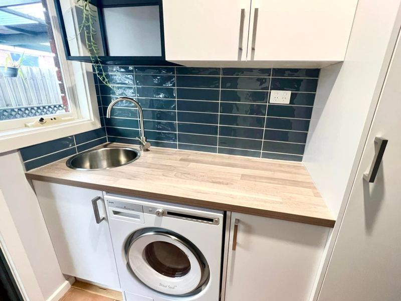 Laundry with teal subway splashback and timber benchtop